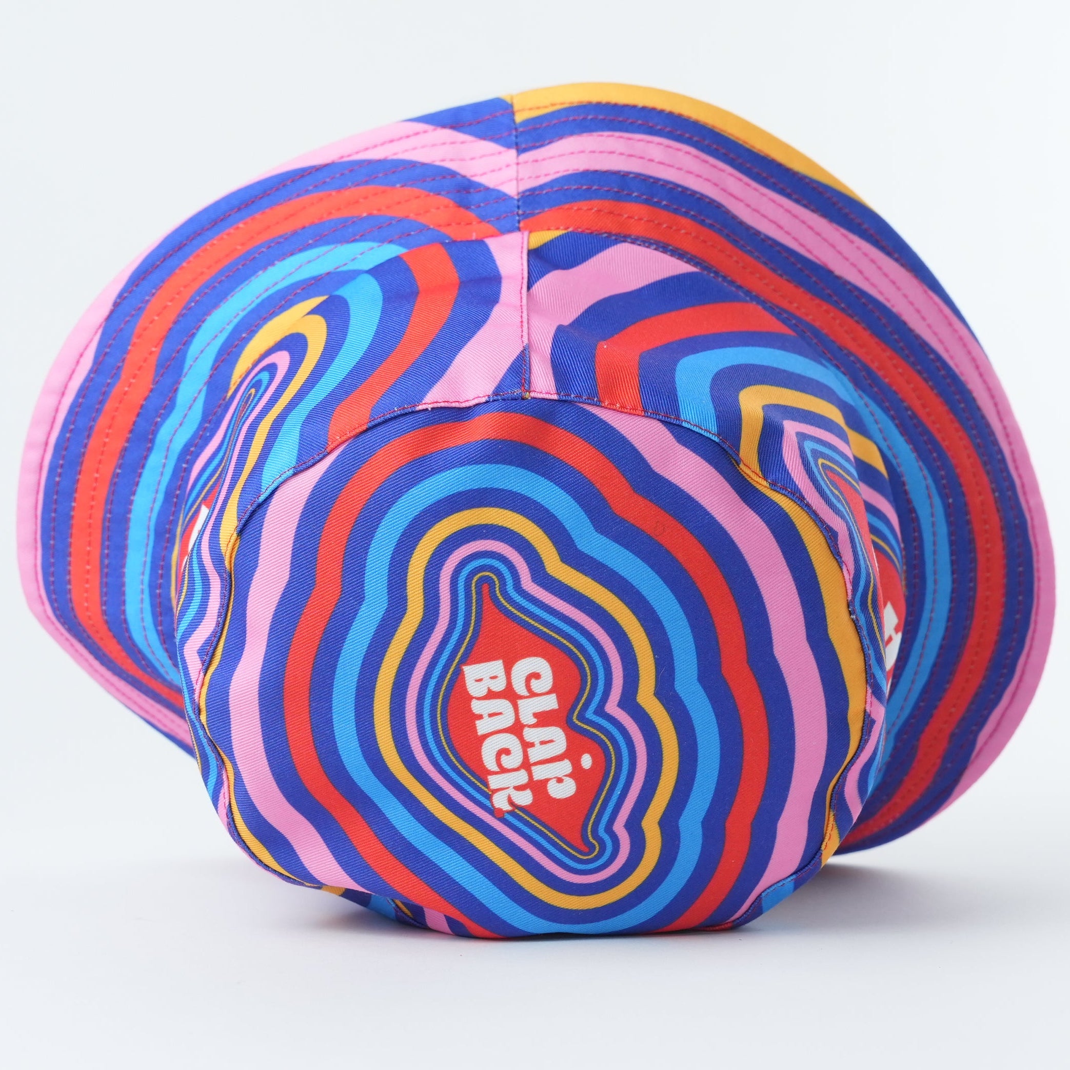 A multicolor patterned baseball cap with concentric wavy stripes in pink, blue, orange, yellow, and purple, featuring a red and white 'Grip the Ball' logo on the front, set against a plain white background.