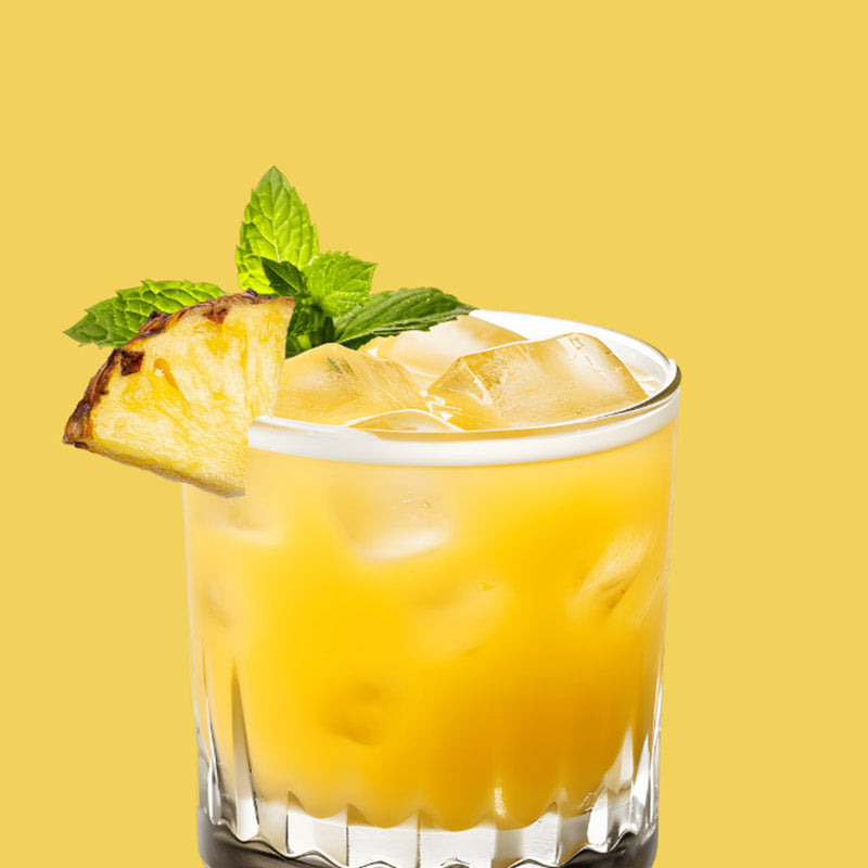 Glass of ClapBack Pick Me  Pineapple wine cocktail with a slice of pineapple and mint leaves on a yellow background