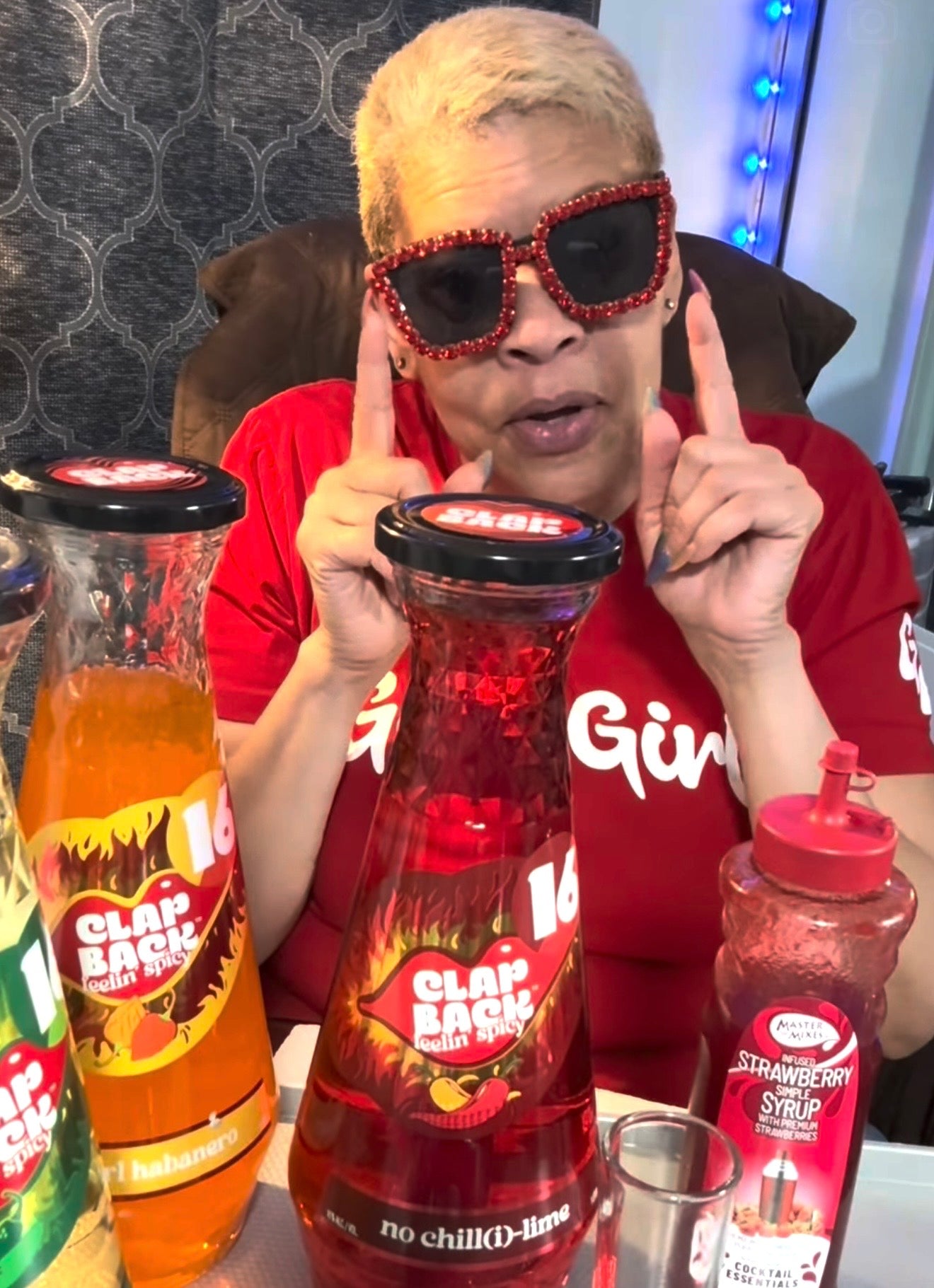 Person wearing red sunglasses with black frames, sitting behind a table with Clap Back drinks.