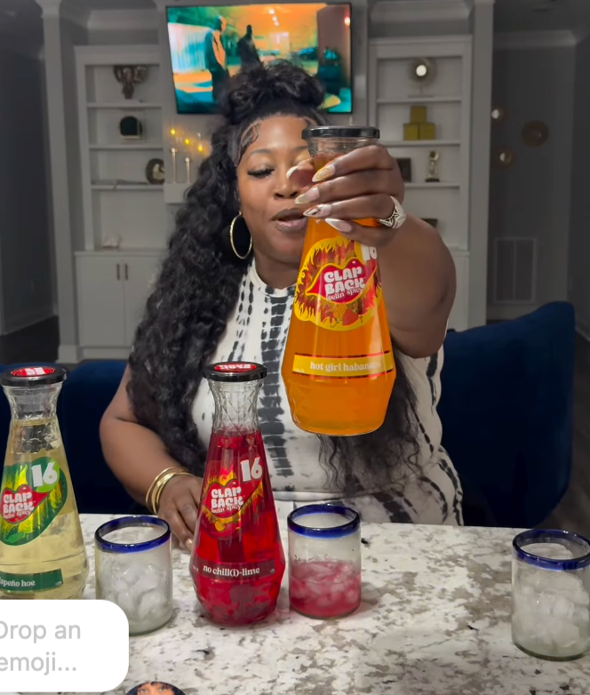 Person holding a glass of hot girl habanero with bottles on a table