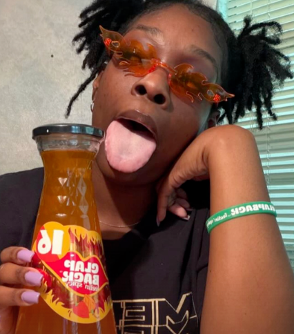 Person holding a bottle of clapback wine with a colorful label, wearing sunglasses and a black shirt.