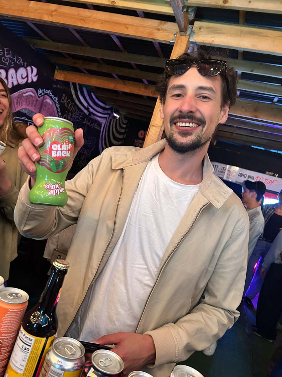 Man holding a can of ClapBack me apple grape wine drink in a casual setting with other people and drinks.
