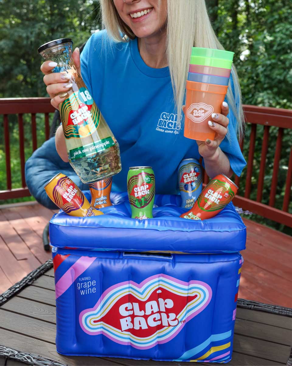Person holding Clap Back drinks and a cooler on a wooden deck